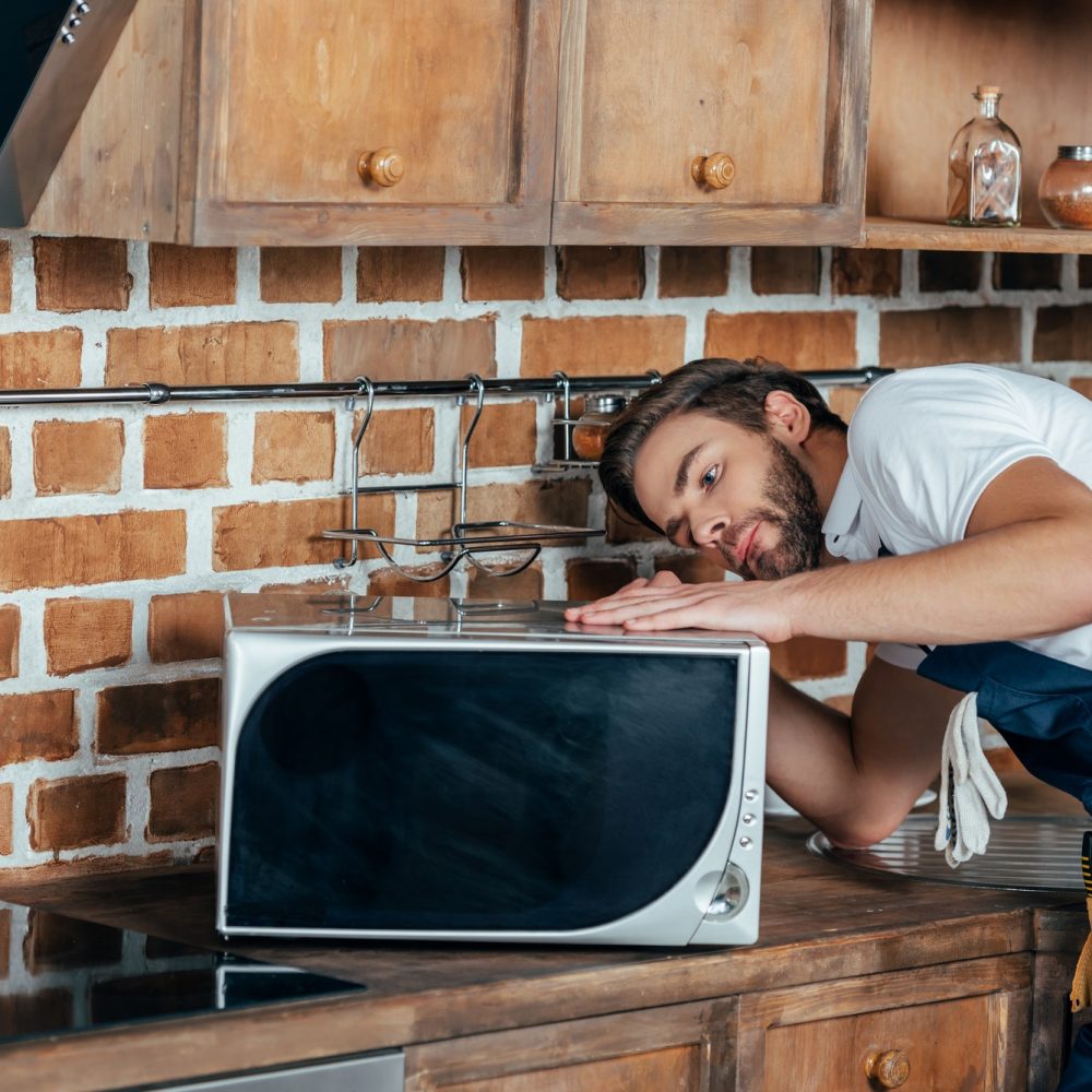 young handyman repairing microwave oven in kitchen
